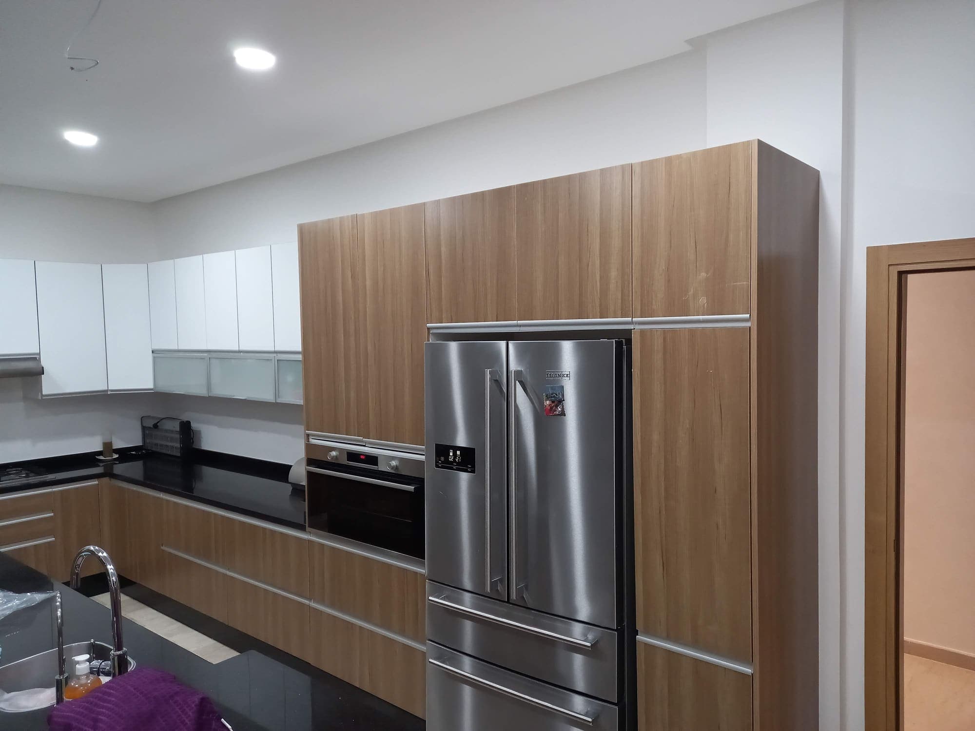 Cuisine avec colonne en bois, réfrigérateur américain en inox et plan de travail noir