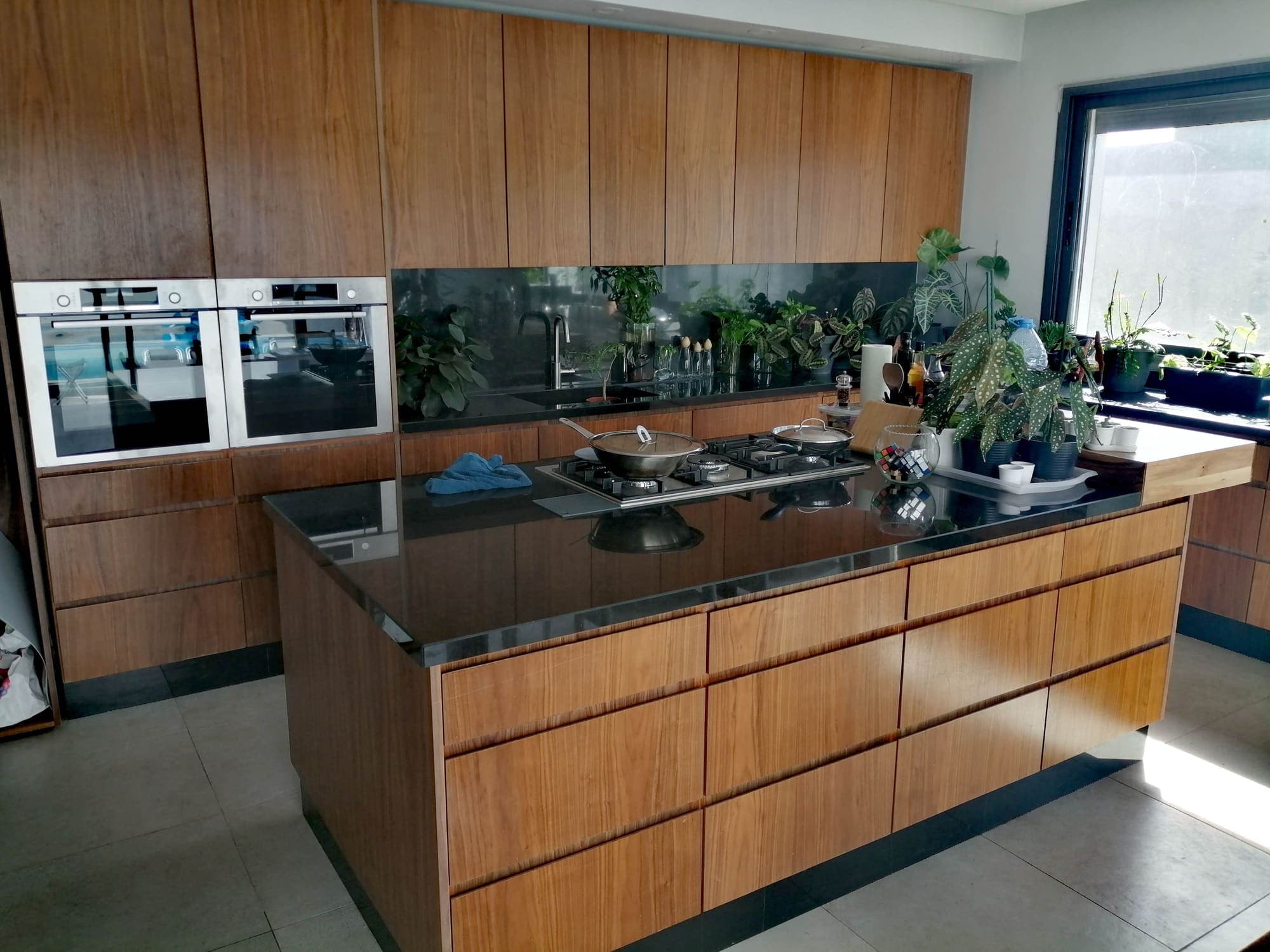 Cuisine avec îlot et façades en bois veiné, plan de travail noir et deux fours encastrés