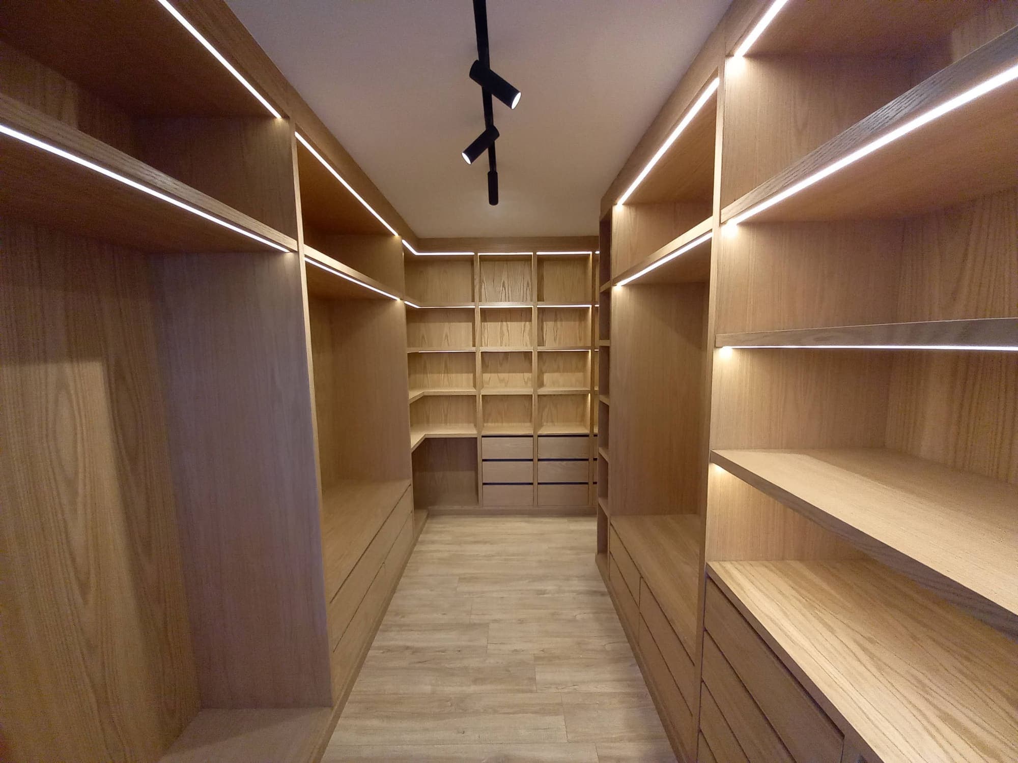 Dressing en bois clair avec étagères, tiroirs et éclairage linéaire