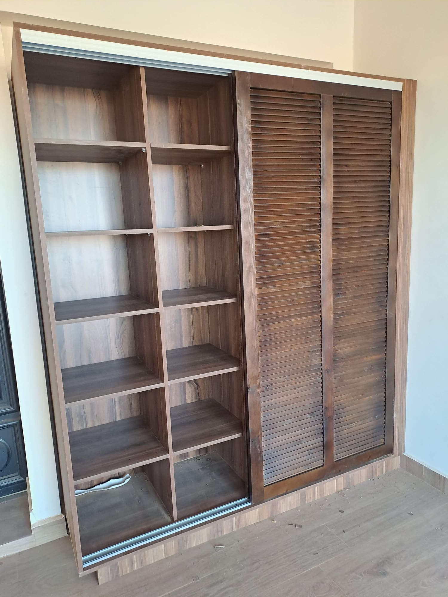 Placard coulissant en bois foncé avec porte à lames et rangements ouverts